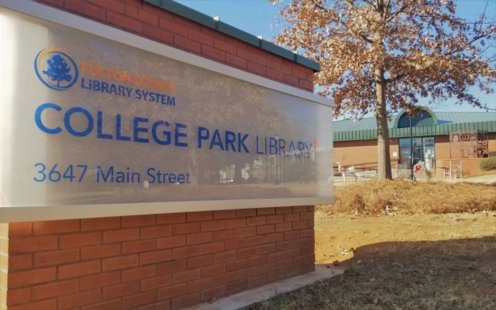 Exterior view of College Park Library sign on brick wall with autumn tree and building in background
