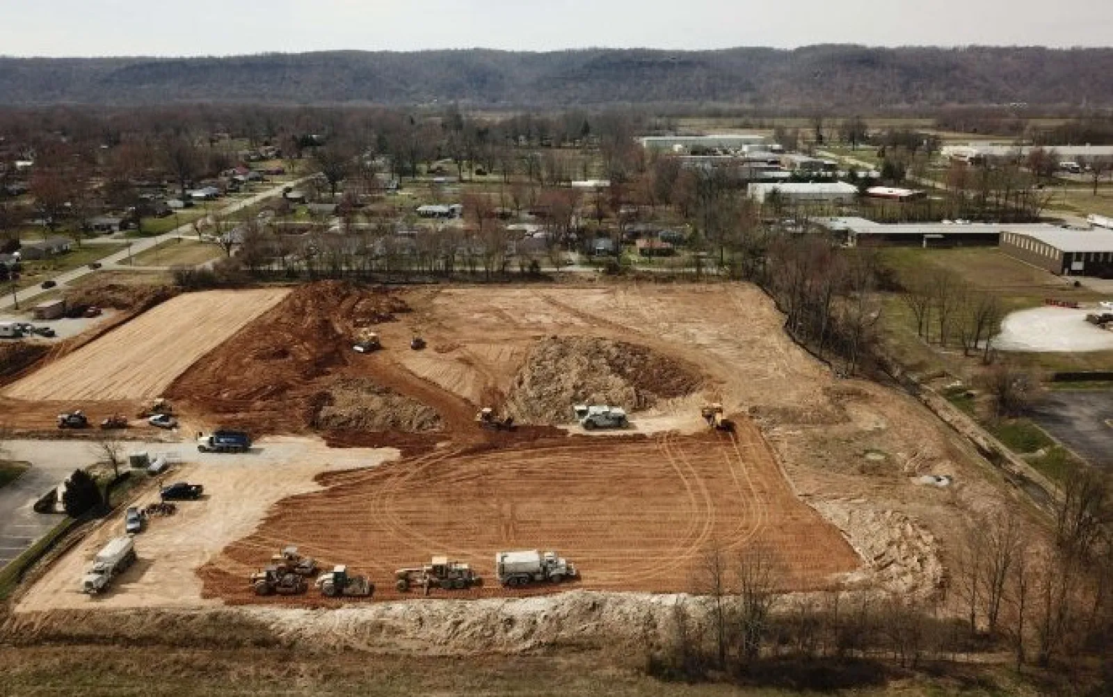 Aerial view of large construction site with trucks and machinery preparing land in a suburban area.