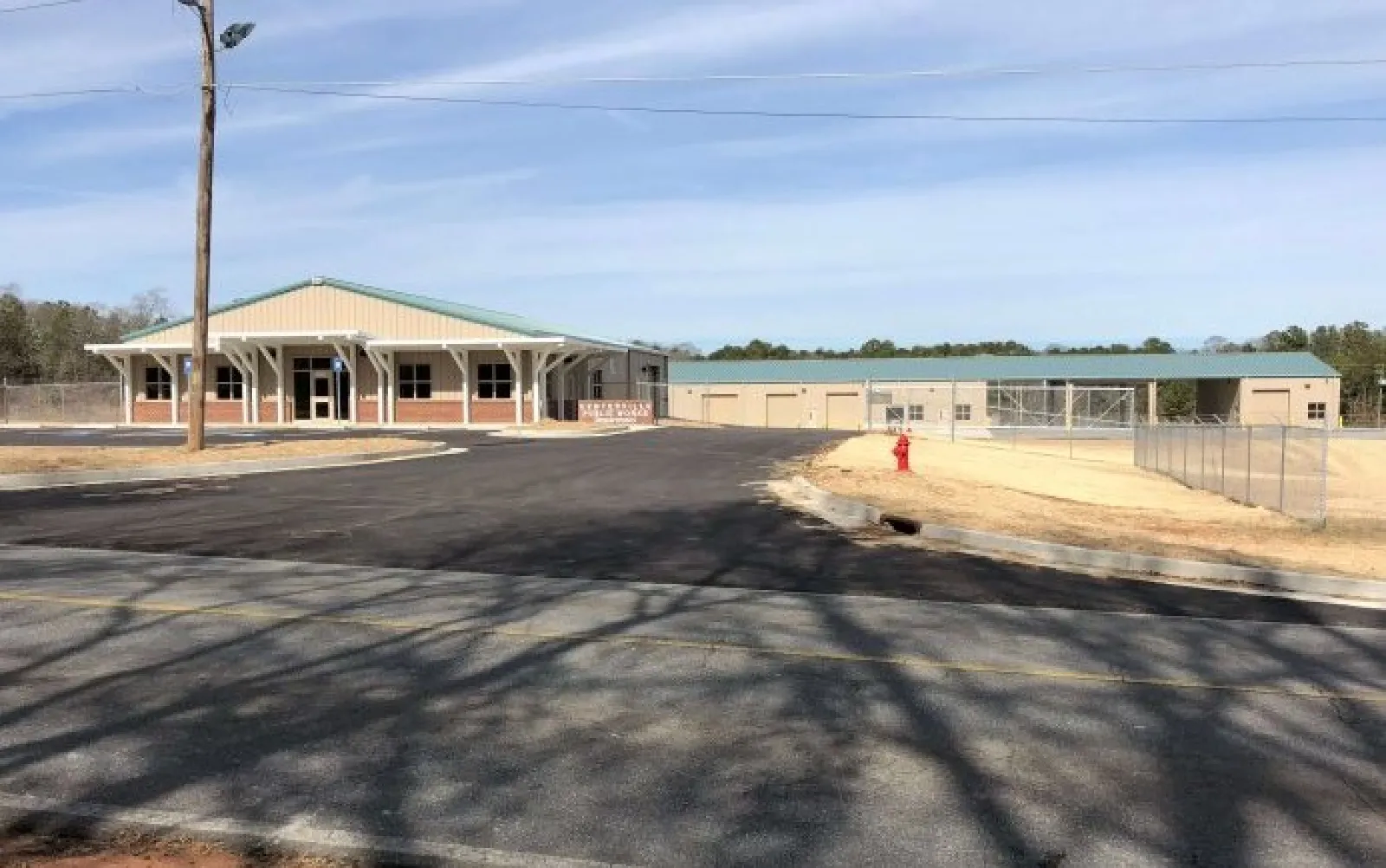 Newly constructed single-story building with green roof, large paved parking lot, and fenced area under clear sky.