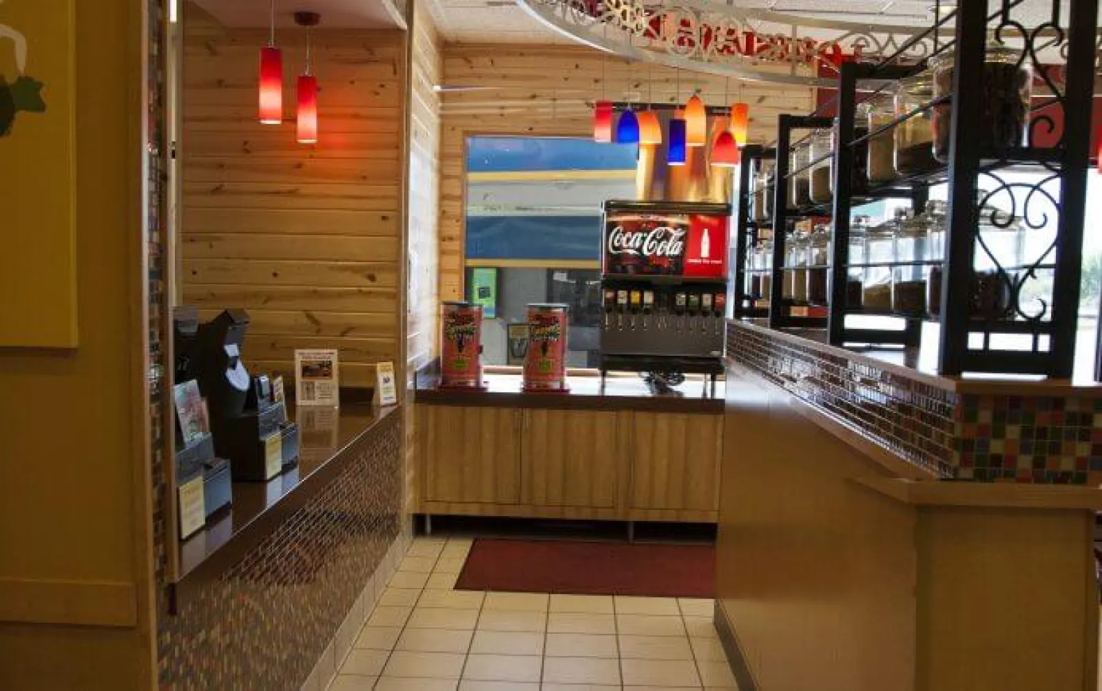 Interior of a restaurant self-service drink station with Coca-Cola dispenser and colorful hanging lights.