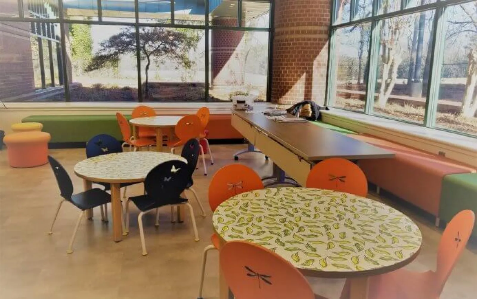 Bright modern room with round tables featuring leaf designs and colorful chairs under large windows with natural light.