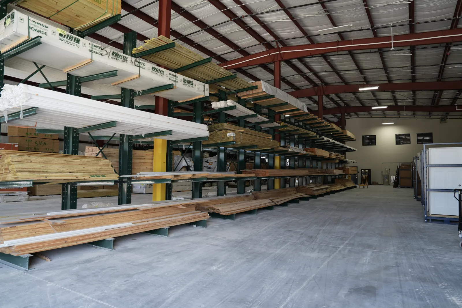 Interior view of a lumber warehouse with stacked wood planks and boards on industrial shelves.