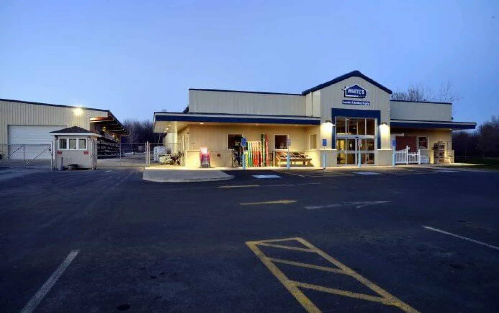 Exterior view of White's supply store building illuminated at dusk with empty parking lot in front.