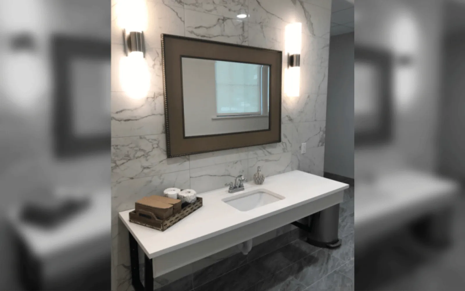 Modern bathroom vanity with white countertop, rectangular sink, framed mirror, and marble wall tiles with sconces.