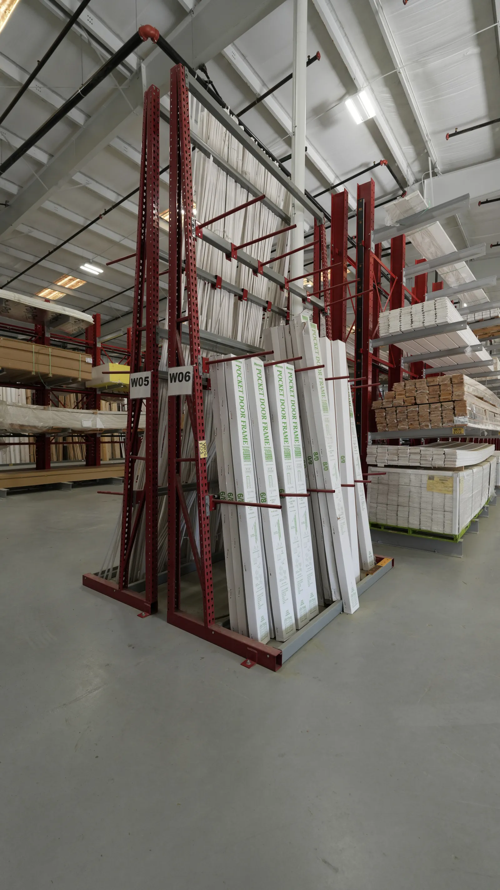 Warehouse racks storing boxed pocket door frames and lumber in an organized industrial setting.