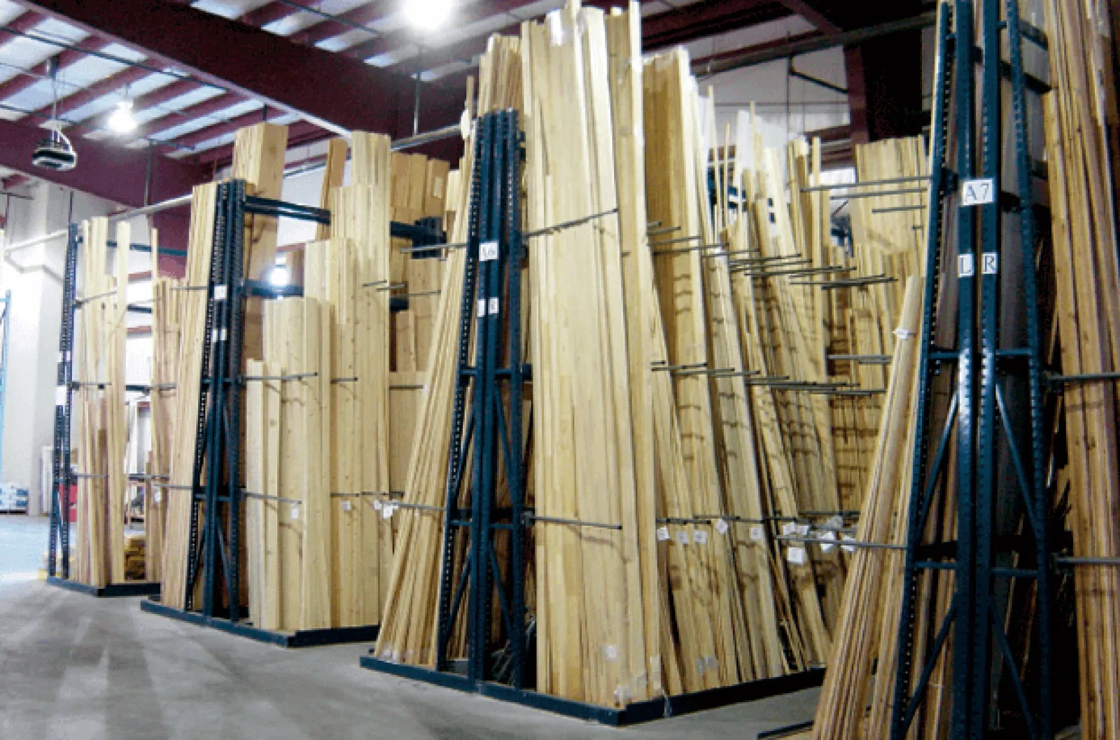 Large stacks of wooden planks stored upright in an organized warehouse with high ceilings and bright lighting