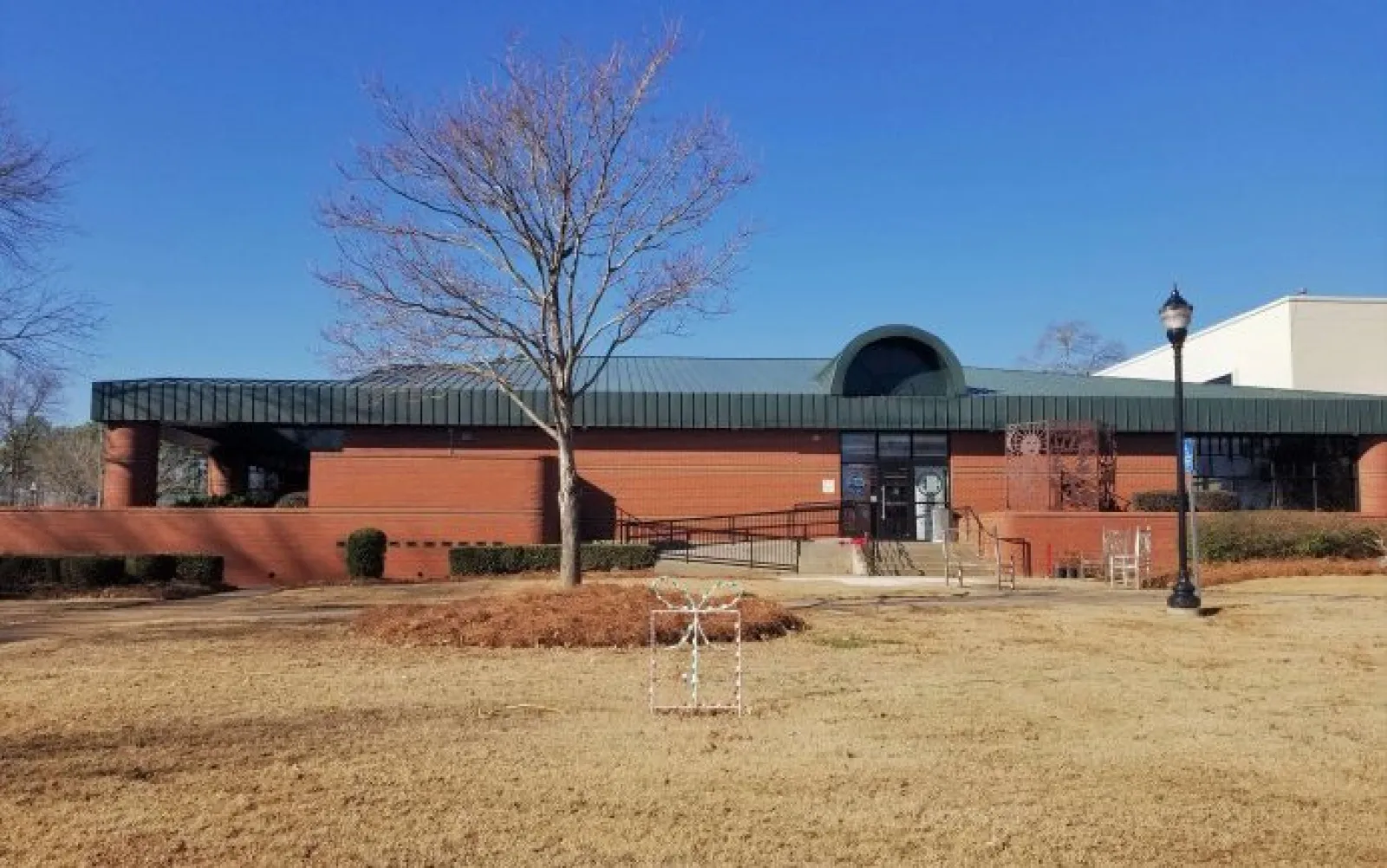Brick building with green roof, leafless trees, and dry grass under clear blue sky on a sunny day