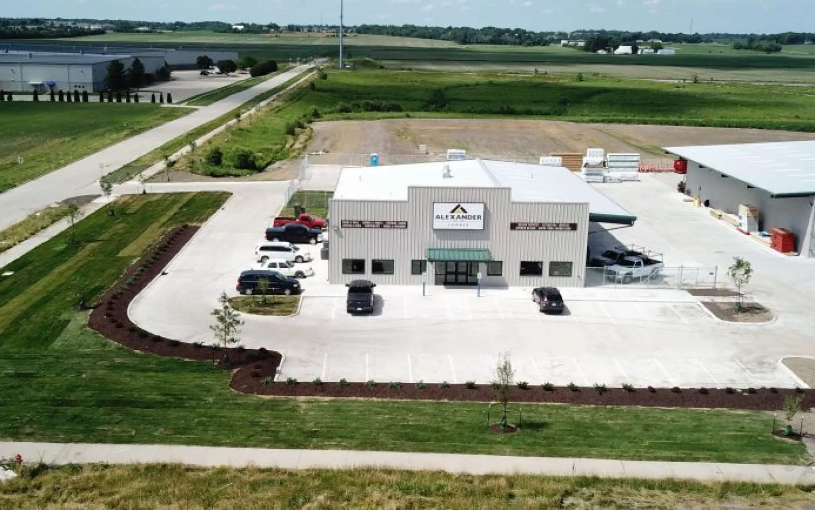 Aerial view of Alexander building with parking lot, surrounding greenery, and rural landscape under blue sky.