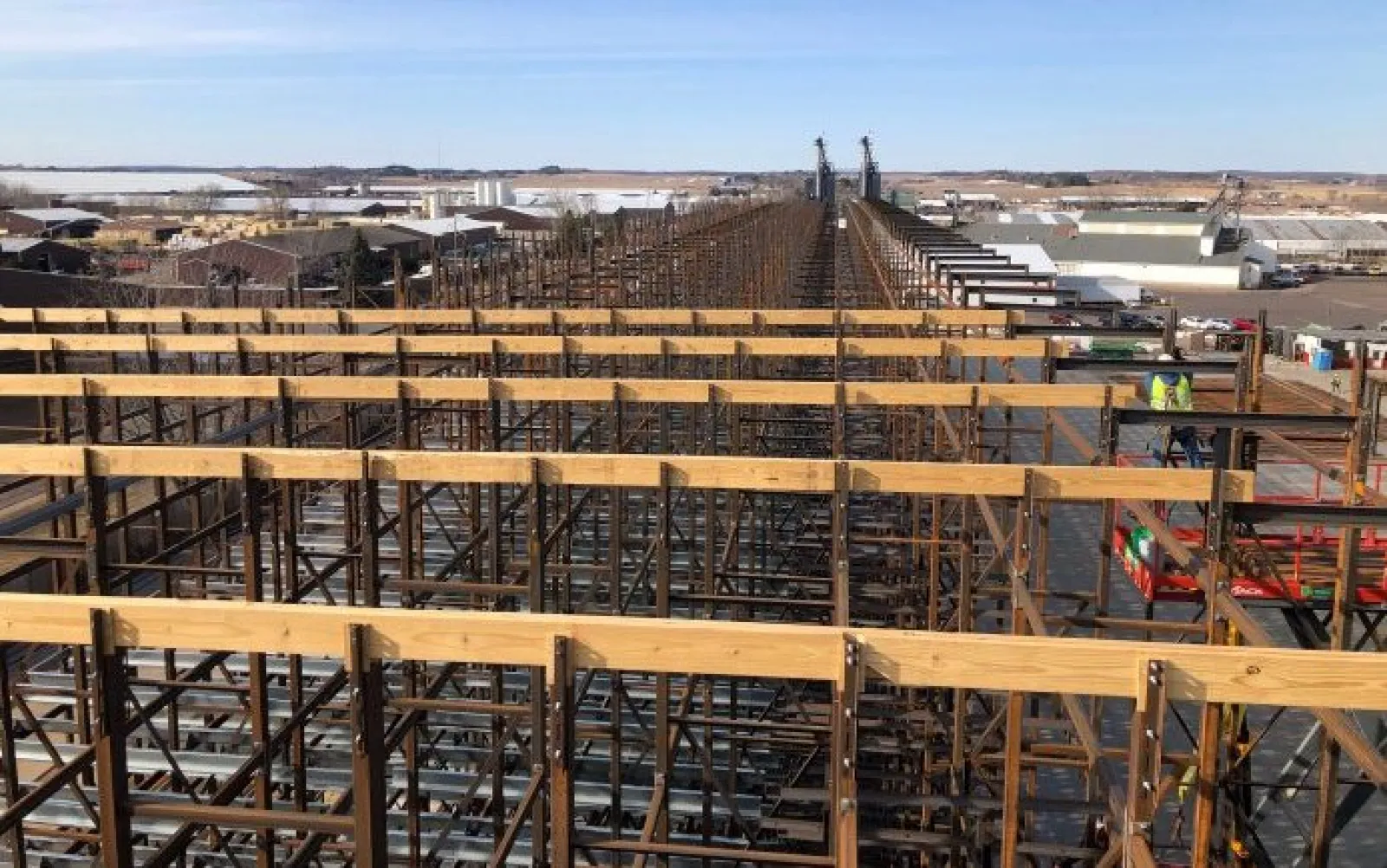 Large industrial wooden scaffolding structure under clear sky with workers and buildings in the background