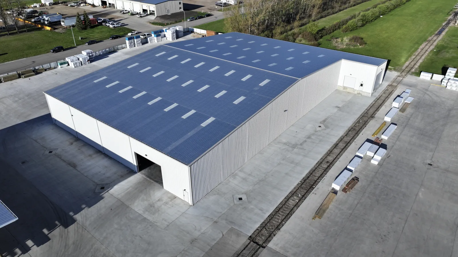 A large industrial warehouse with a blue roof and surrounding concrete yard in an open area.