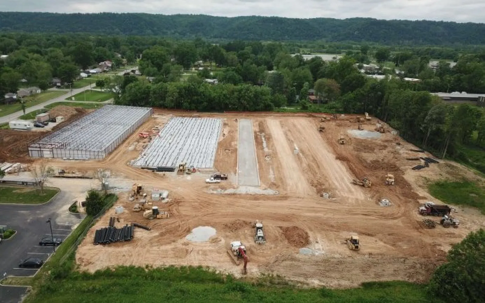 Aerial view of a construction site with machinery, foundation work, and surrounding greenery.