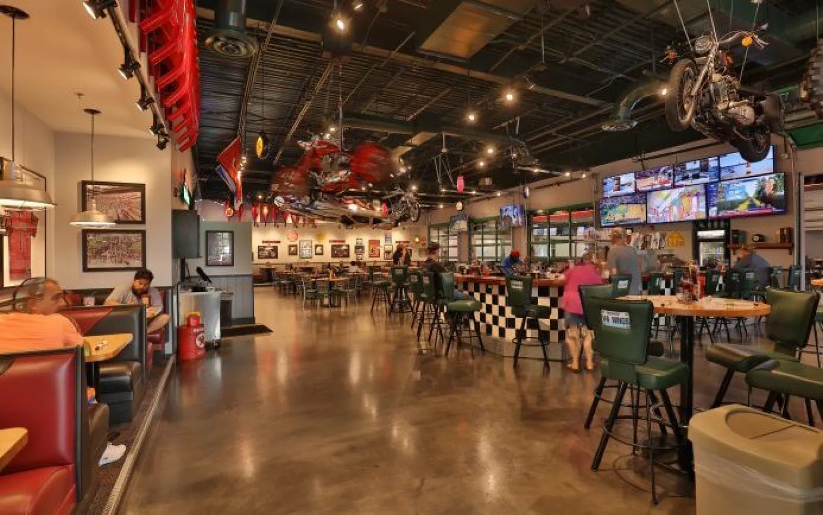 Spacious motorcycle-themed bar and restaurant with patrons, multiple TVs, and unique decor including hanging motorcycles.