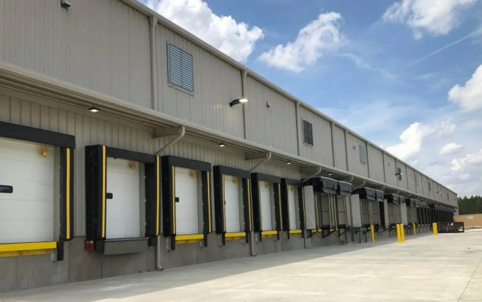 Row of industrial warehouse loading docks with closed dock doors and clear blue sky above.
