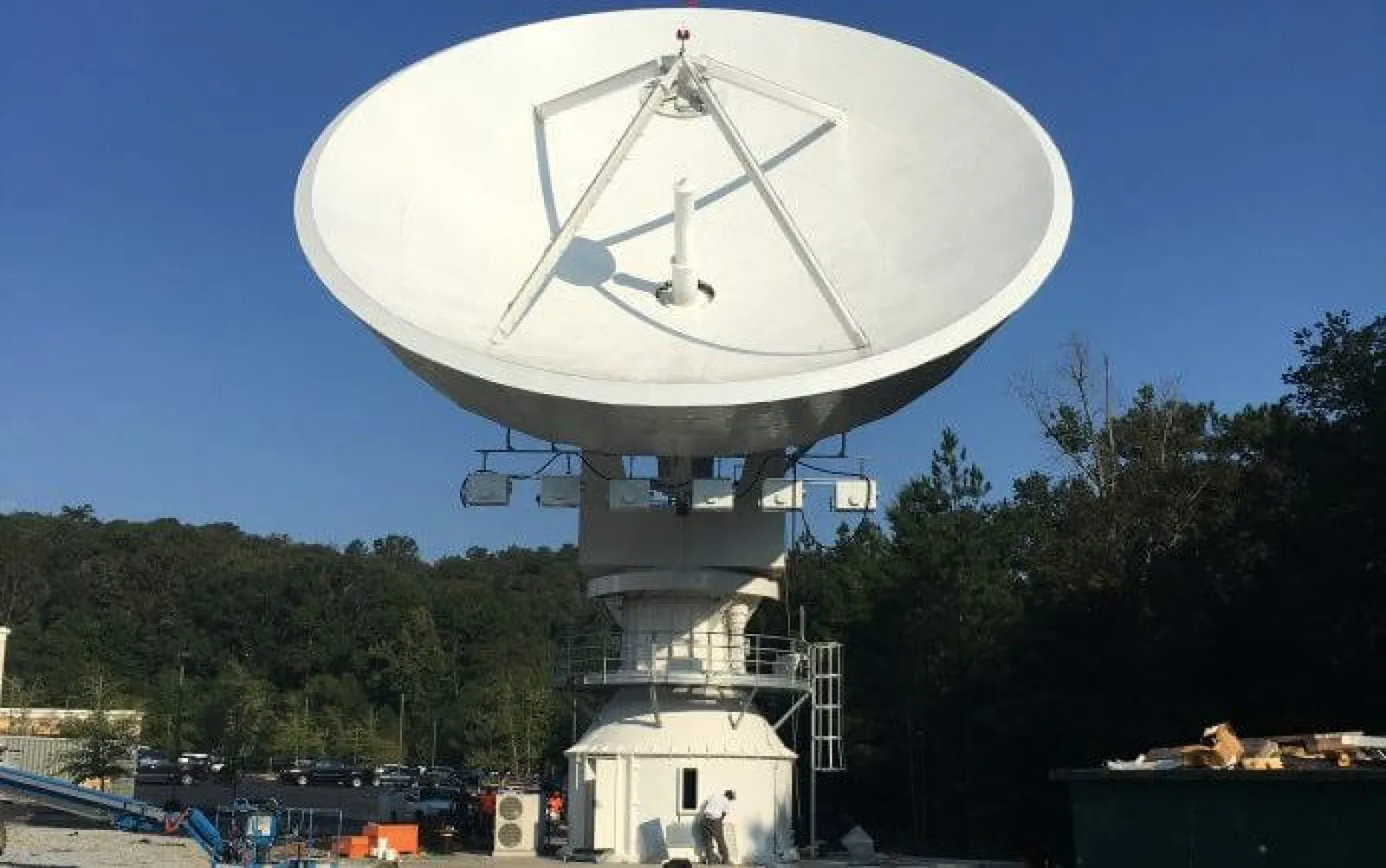 Large white satellite dish antenna mounted outdoors with trees and clear sky in background