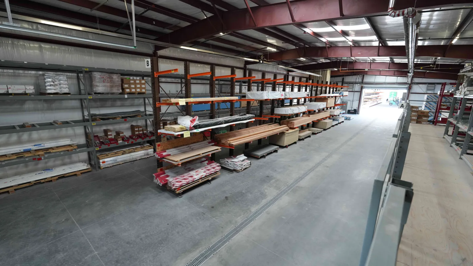 Warehouse interior with metal racks holding wood planks and building materials in an organized industrial space.