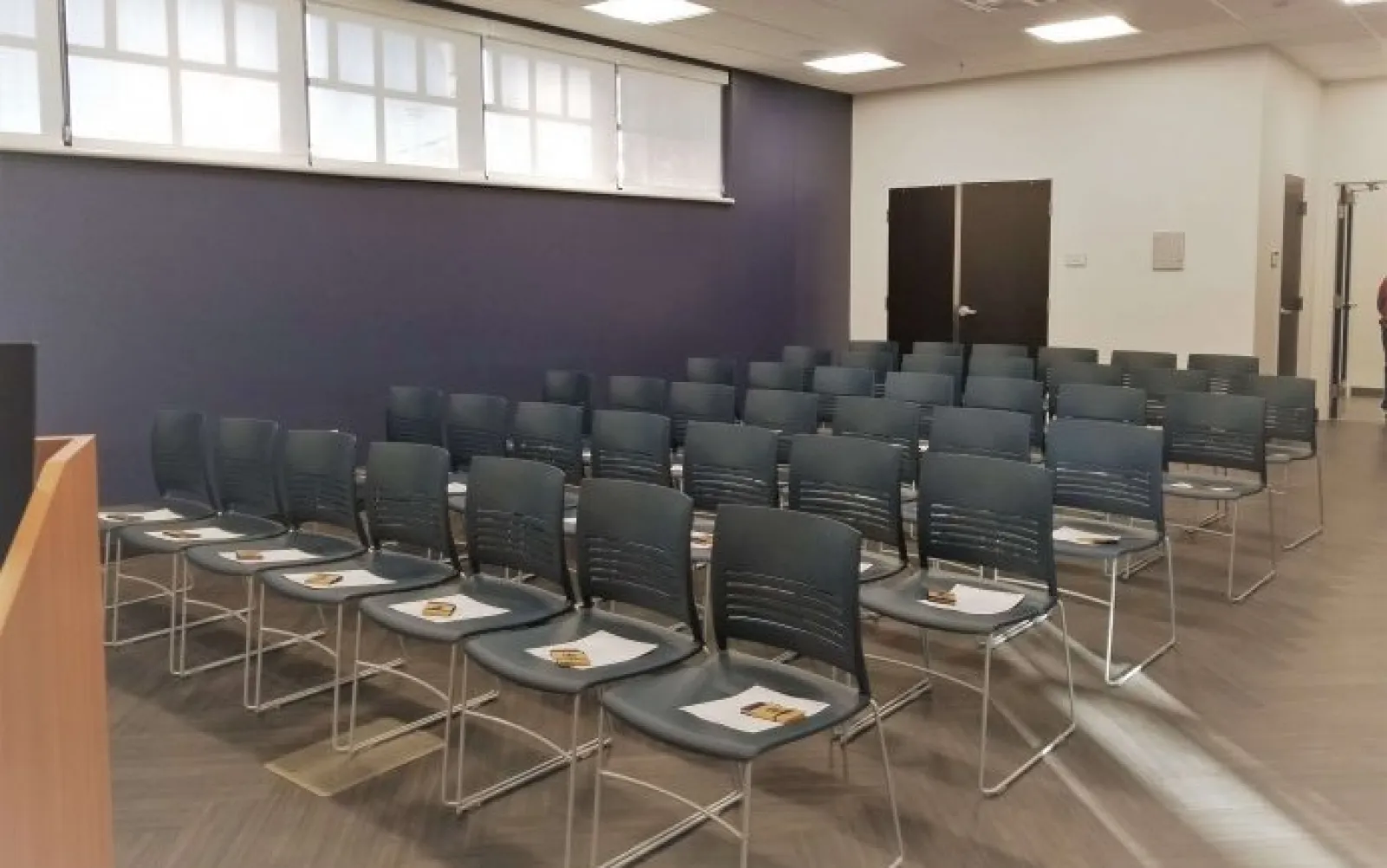 Empty conference room with rows of black chairs and papers on seats, ready for an event or presentation.