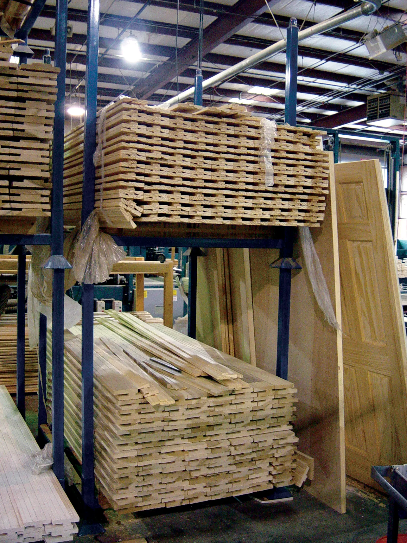 Stacks of wooden planks and doors stored on metal racks inside a woodworking factory warehouse.