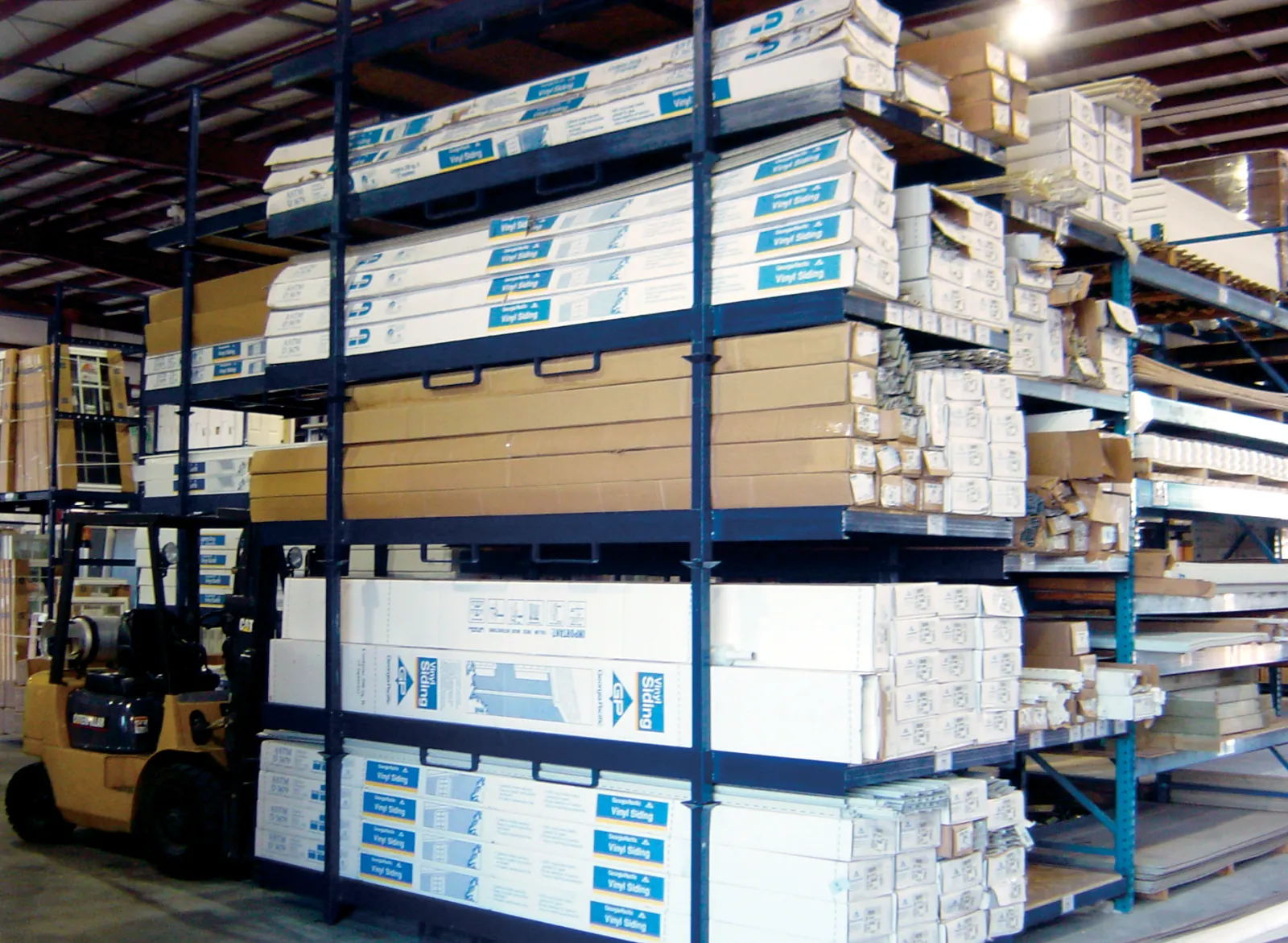 Warehouse shelving stocked with boxed vinyl siding and construction materials with forklift nearby
