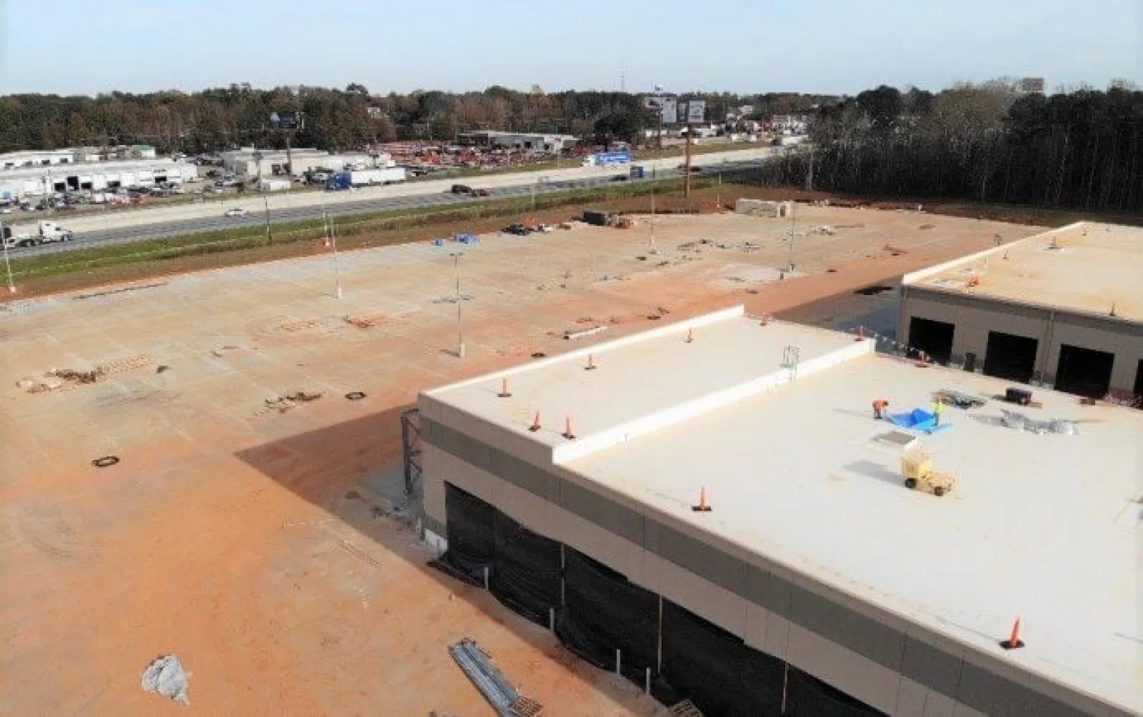 Aerial view of a large construction site with two partially built commercial buildings and empty paved area near a highway.