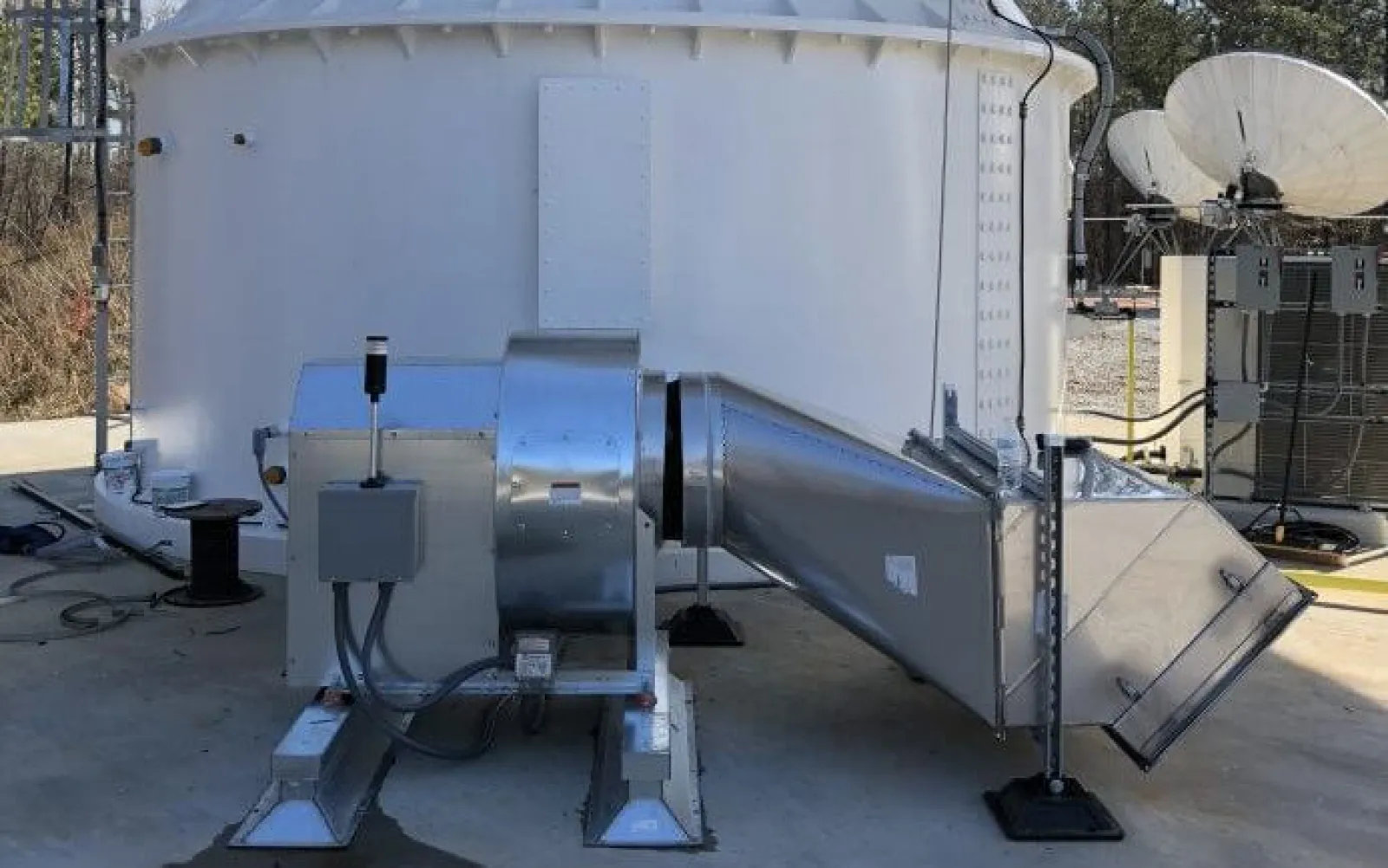 Industrial ventilation system with metal ducts and fan installed on concrete surface outside a building.