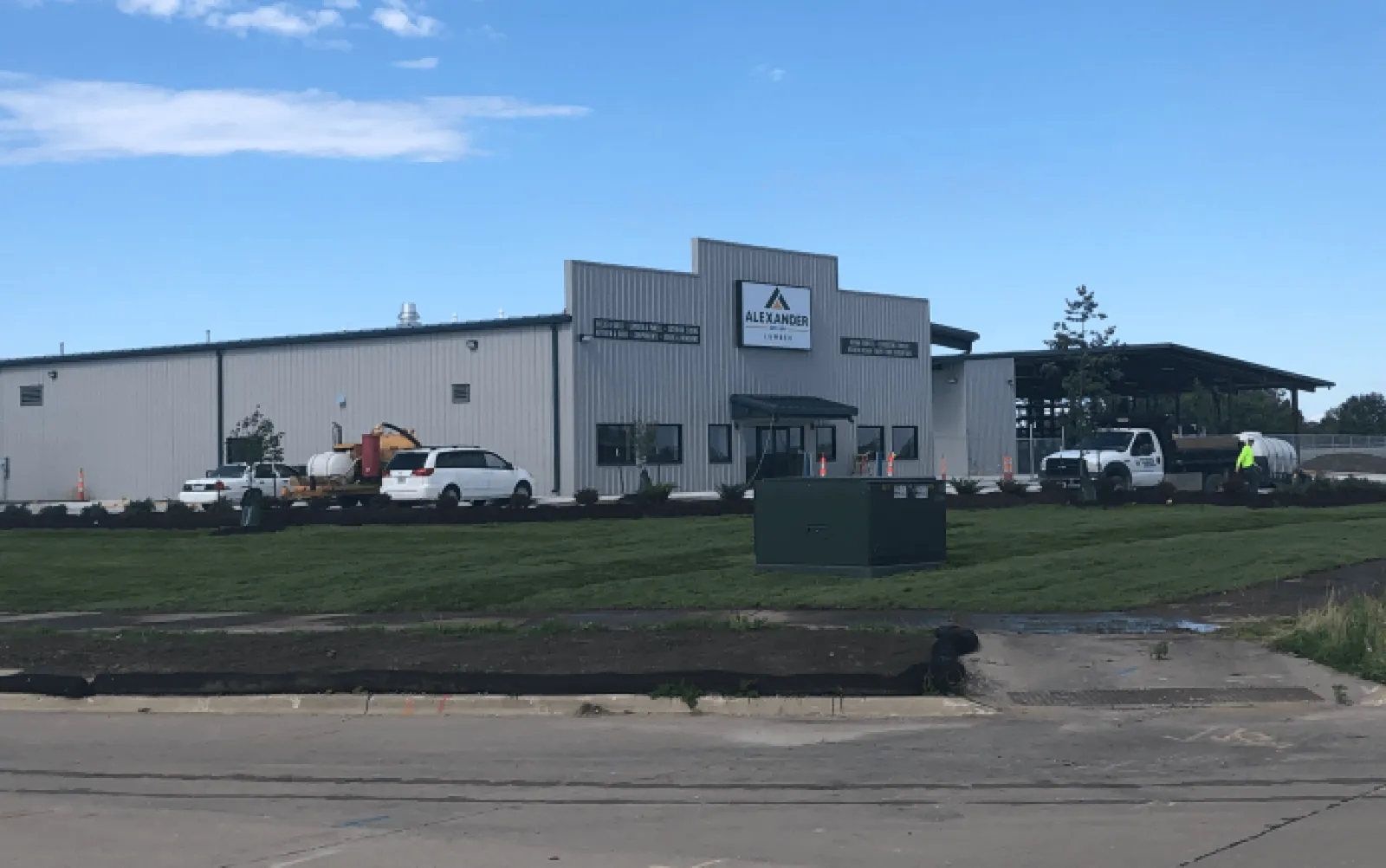 Industrial warehouse building with Alexander Leasing signage, vehicles, and a freshly landscaped lawn under a clear blue sky.