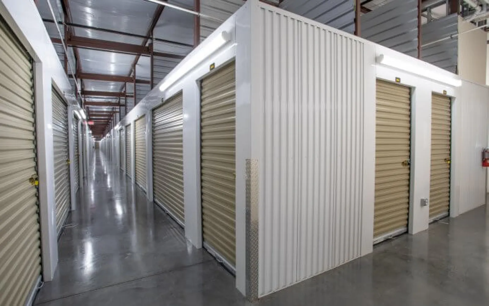 Indoor storage facility with metal roll-up doors along clean polished concrete floors and metal roof framework.