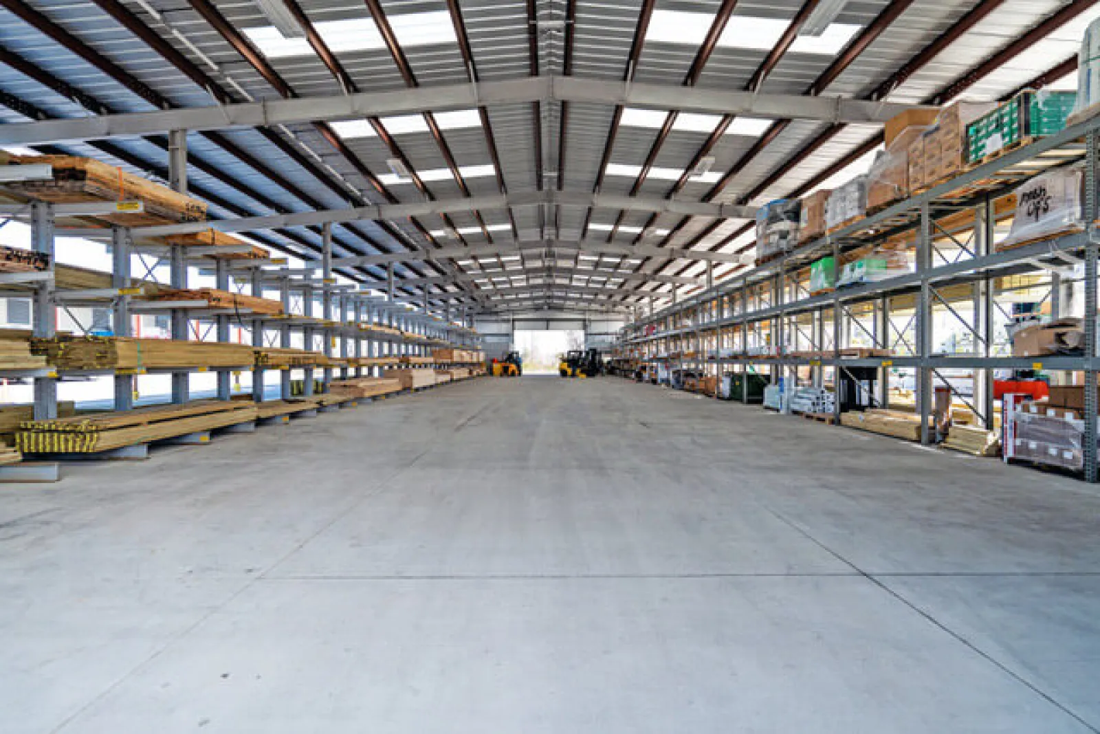 Spacious industrial warehouse interior with high metal shelves stocked with construction materials and equipment.