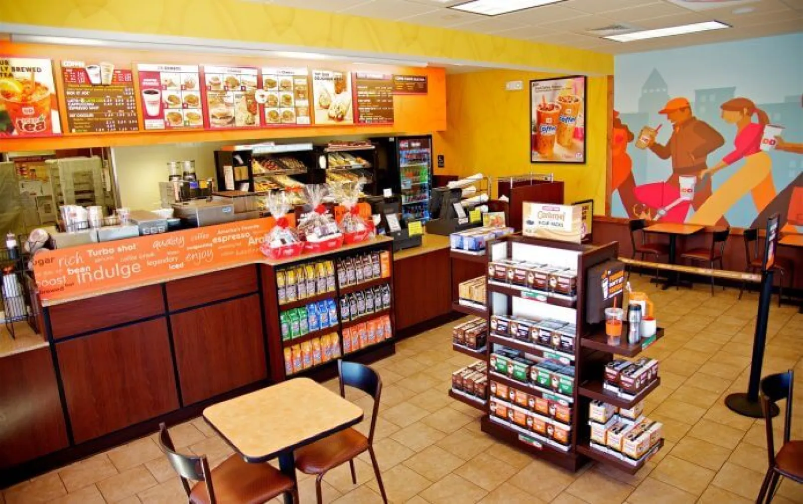 Interior view of a Dunkin' Donuts with menu boards, coffee display, and seating area including mural artwork.