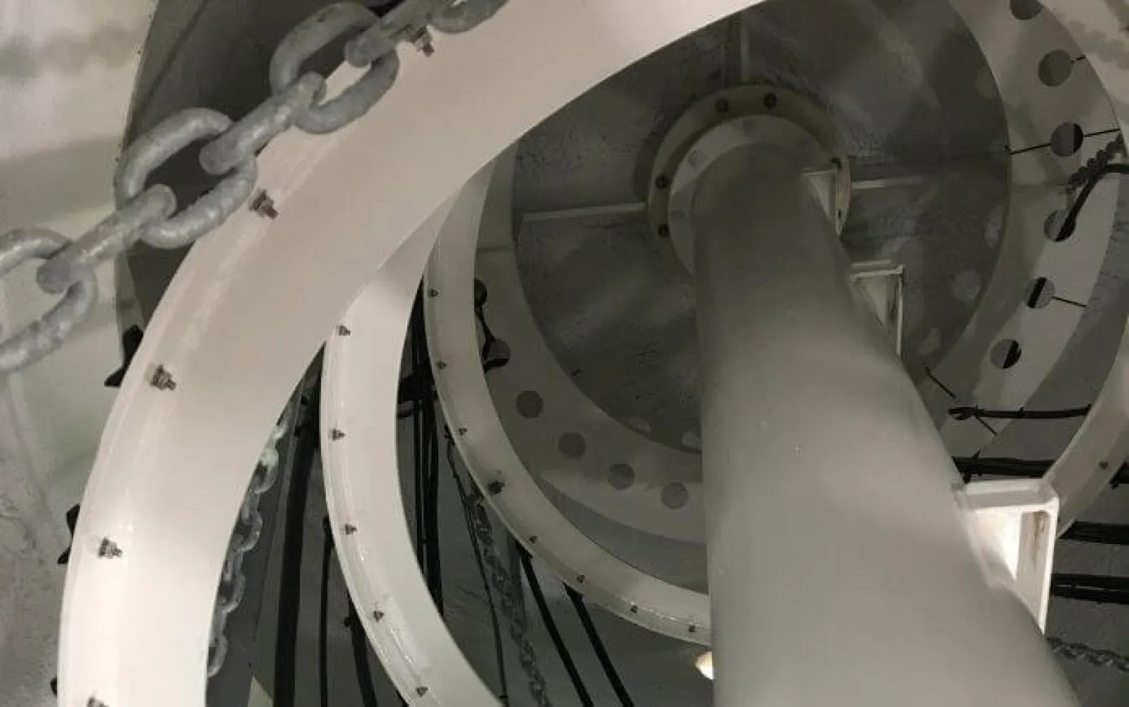 Close-up of industrial white spiral staircase with metal chains and bolts inside a structure.