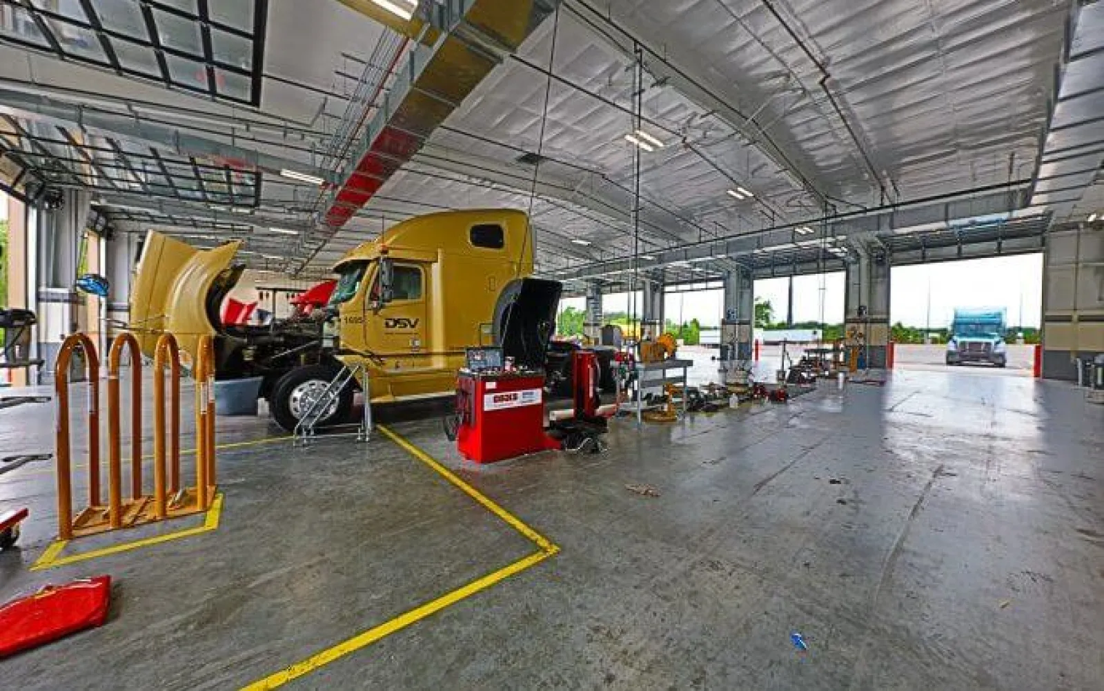 Large yellow truck undergoing maintenance inside a spacious, well-lit truck service garage with equipment and open bays.