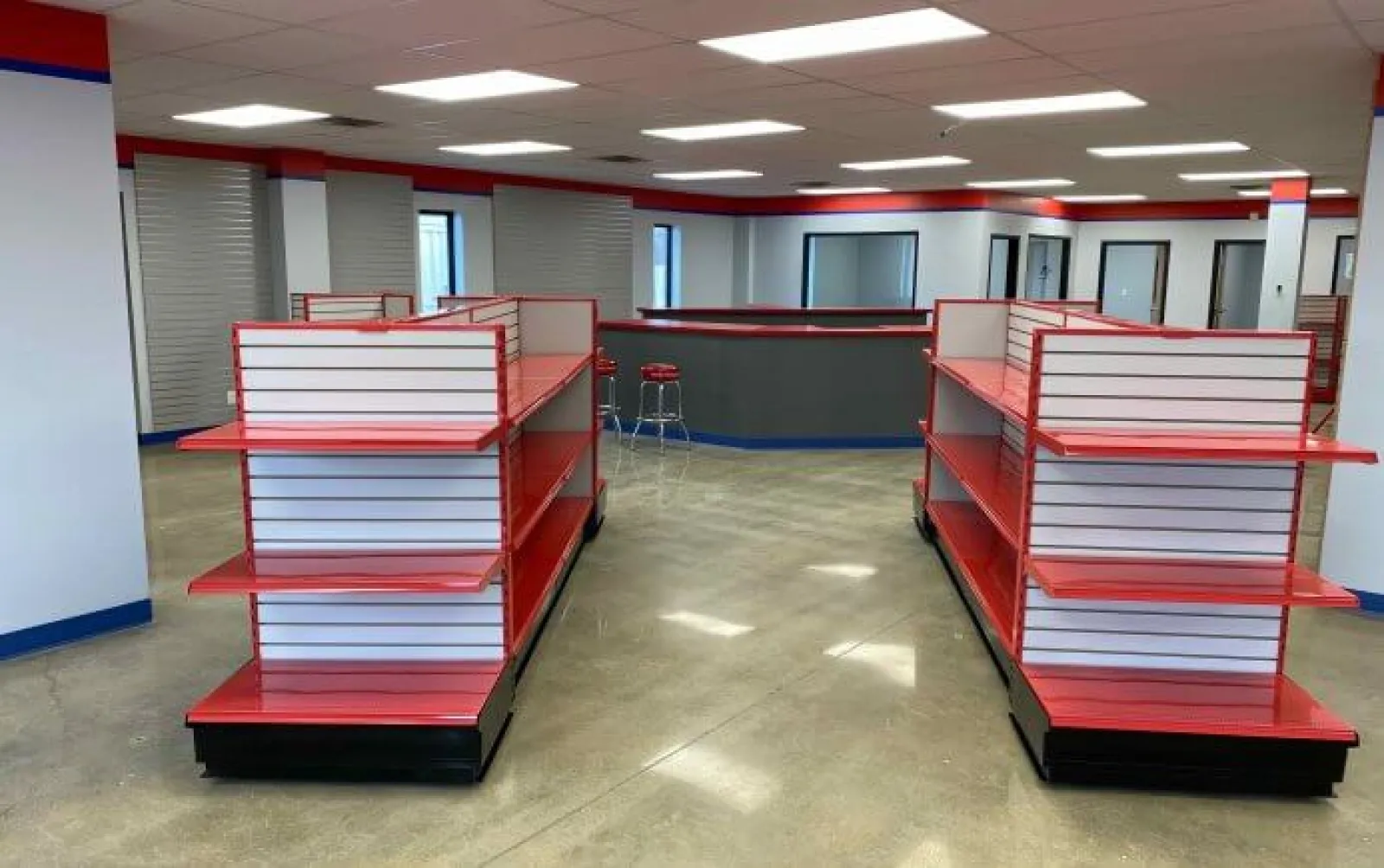 Empty red and white retail display shelves in a spacious, well-lit store interior with polished concrete floors
