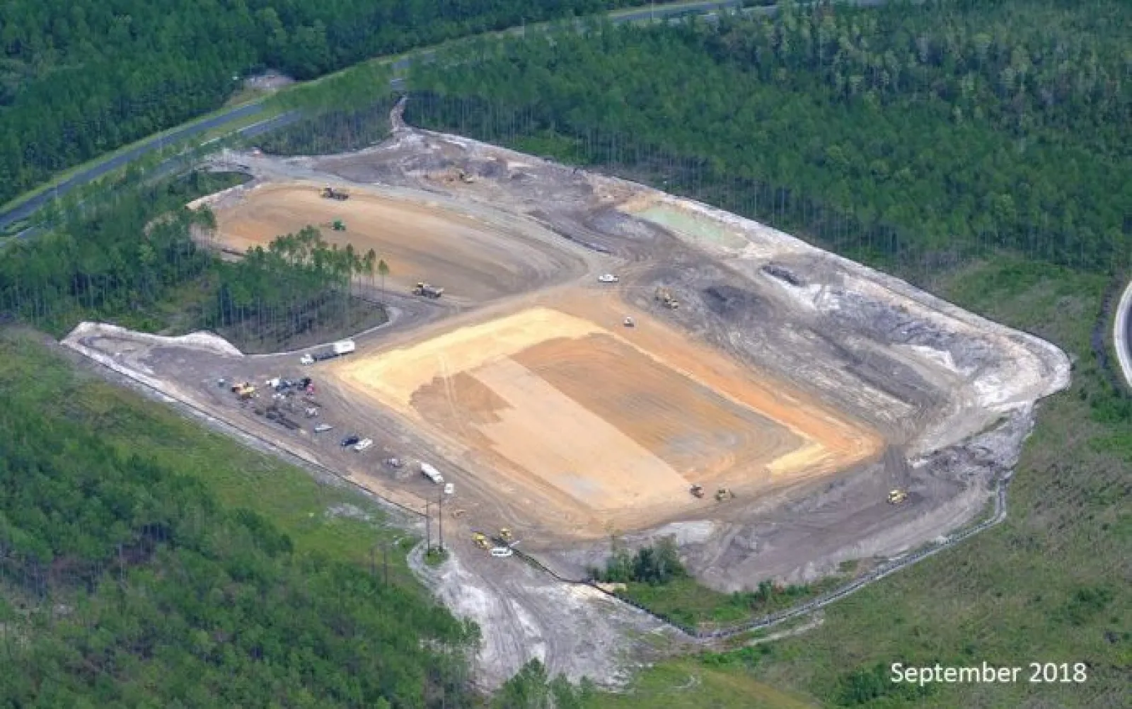 Aerial view of a large construction site cleared in a forested area with earthmoving equipment and vehicles