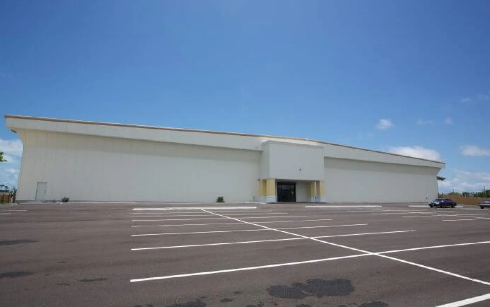 Empty parking lot in front of a large white commercial building under a clear blue sky.