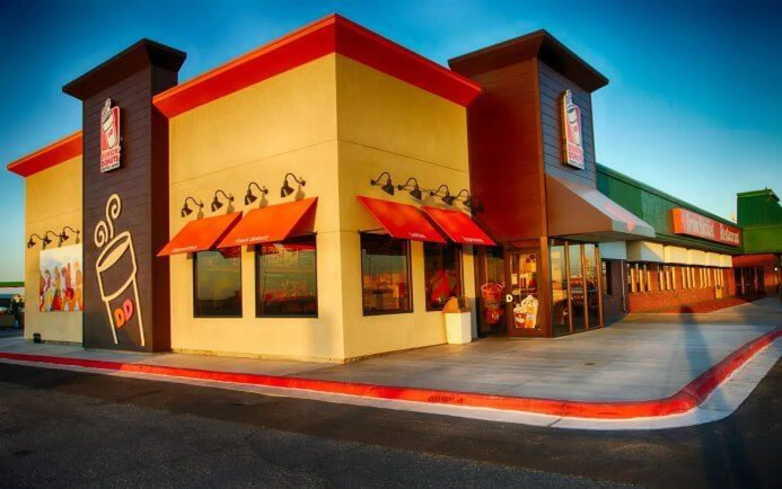 Dunkin' Donuts store exterior with red awnings and signage under clear blue sky at sunset.