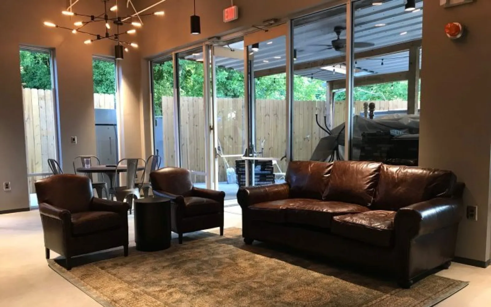 Cozy living room with brown leather sofa, two armchairs, round black table, rug, and large glass doors to outside.