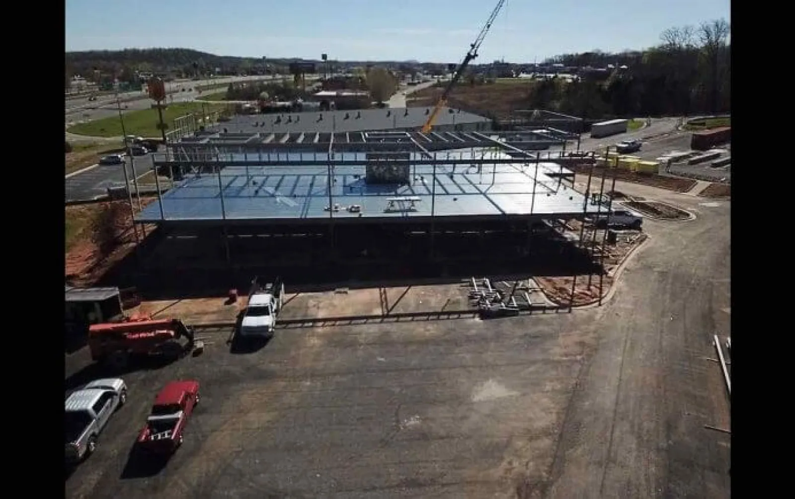 Construction site with steel framework and crane assembling a large commercial building in an industrial area.