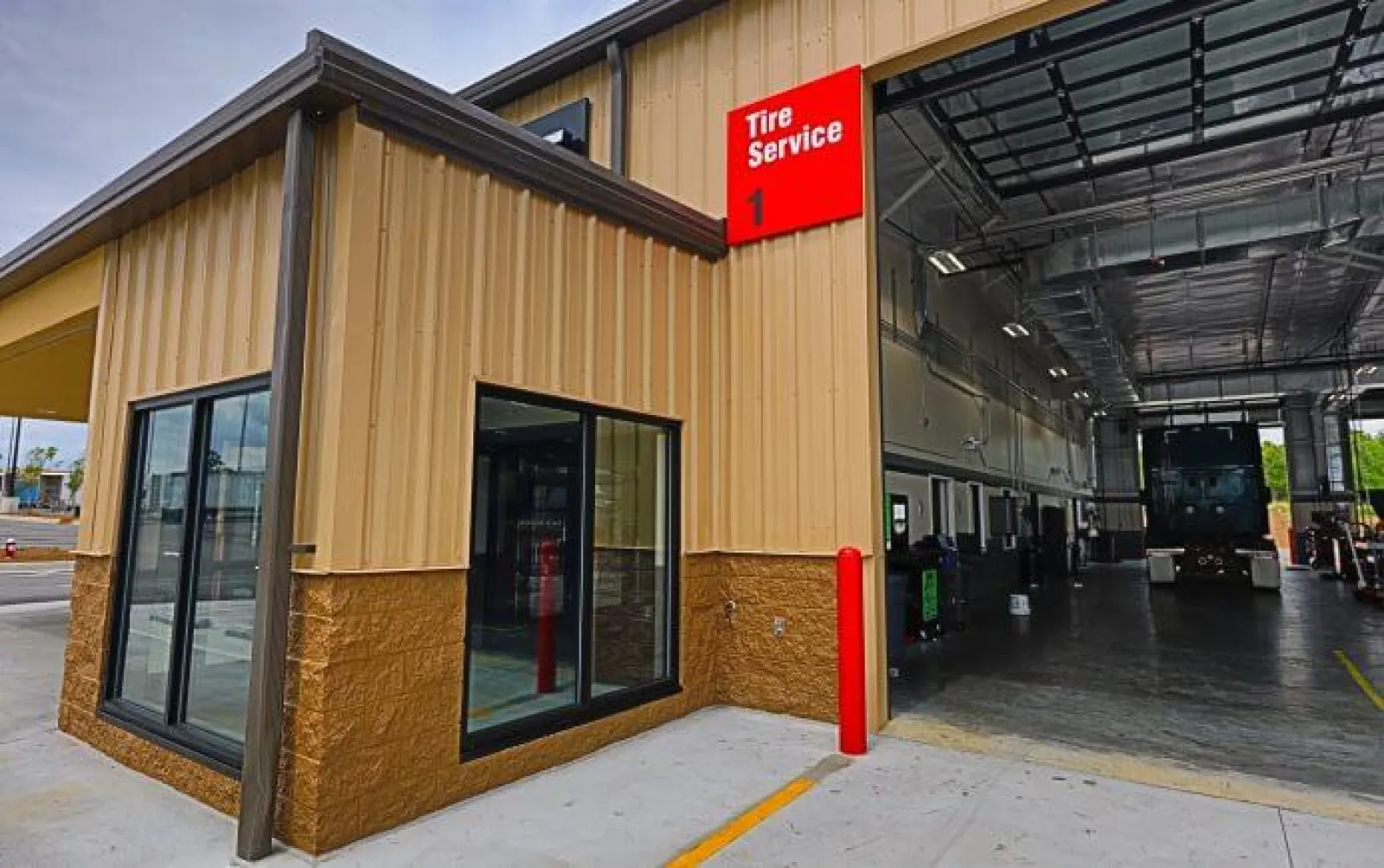 Exterior view of a commercial tire service garage with an open bay and signage under clear sky.