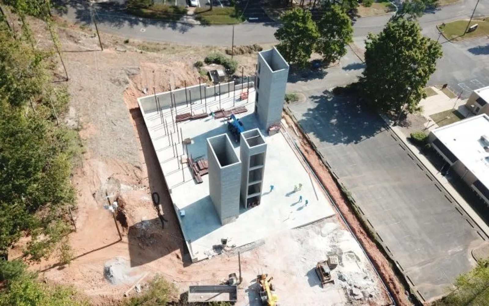 Aerial view of early-stage concrete building construction with tall vertical structures and surrounding cleared land.