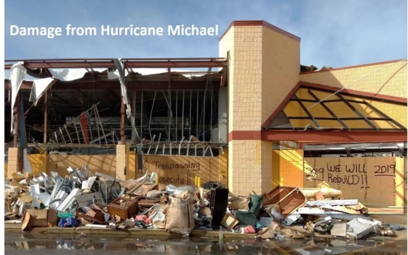 Severely damaged building with debris after Hurricane Michael, with graffiti promising to rebuild in 2019