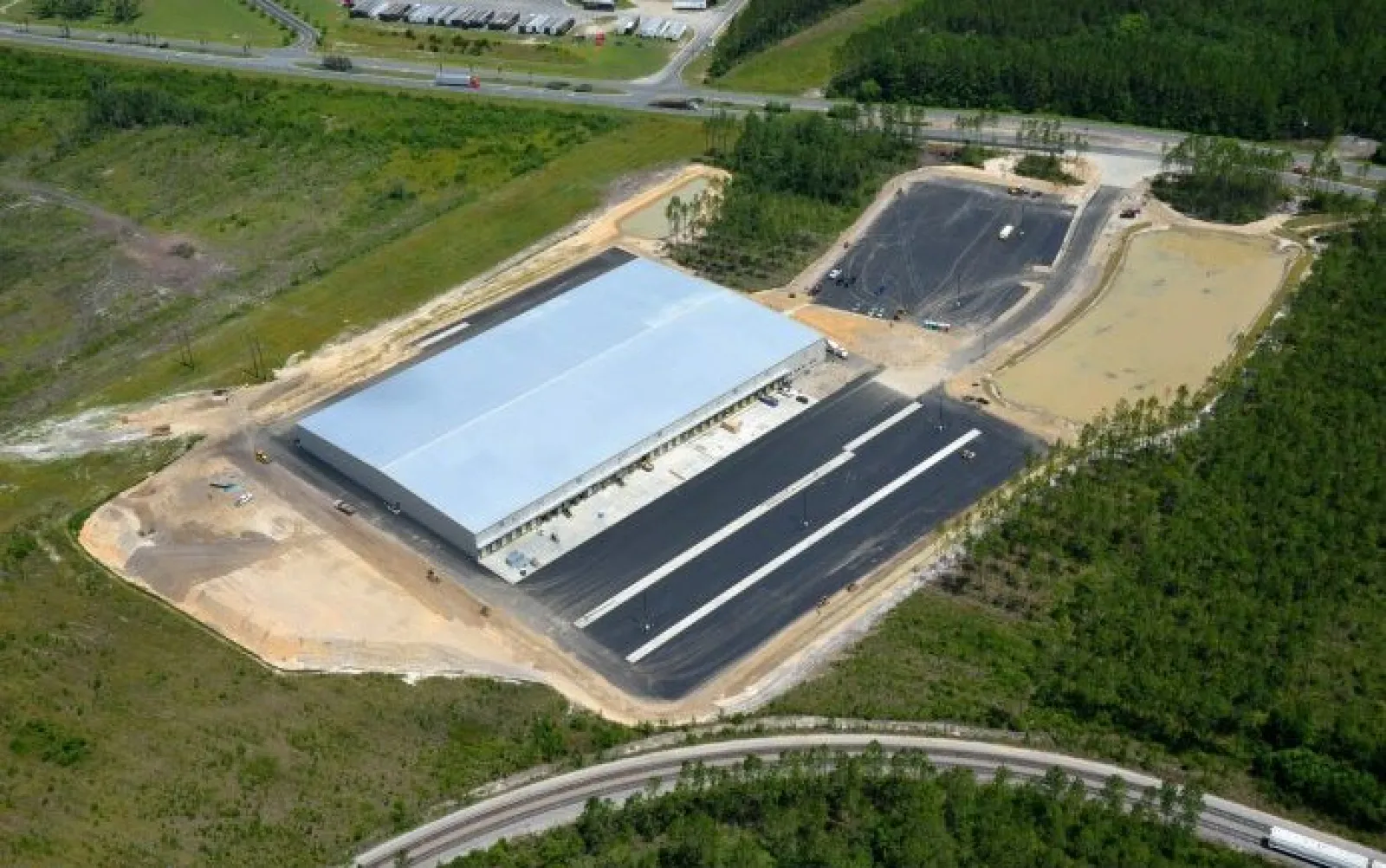 Aerial view of a large industrial warehouse under construction surrounded by greenery and roads.