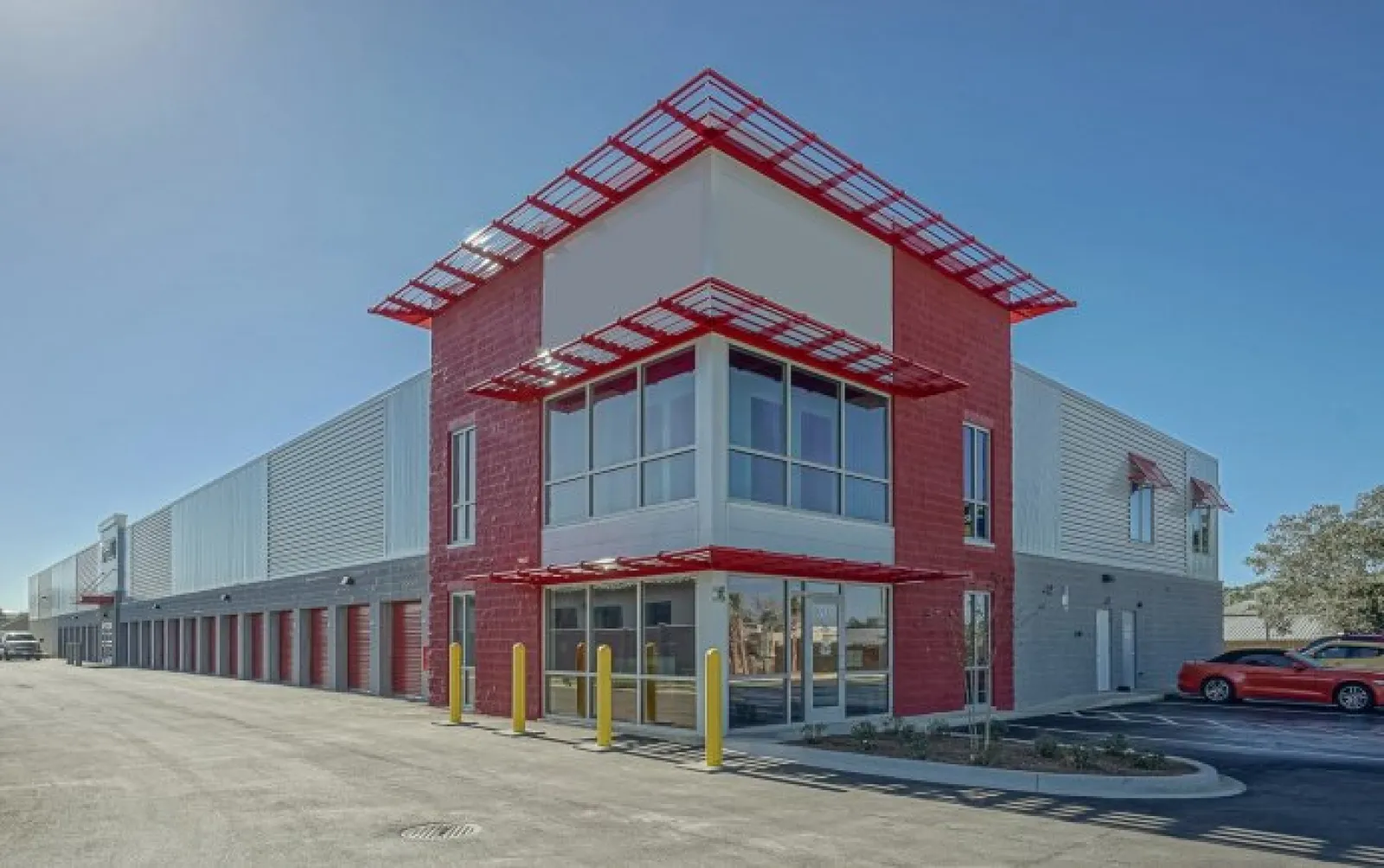 Modern commercial building with red and gray exterior, large windows, and adjacent parking under clear blue sky