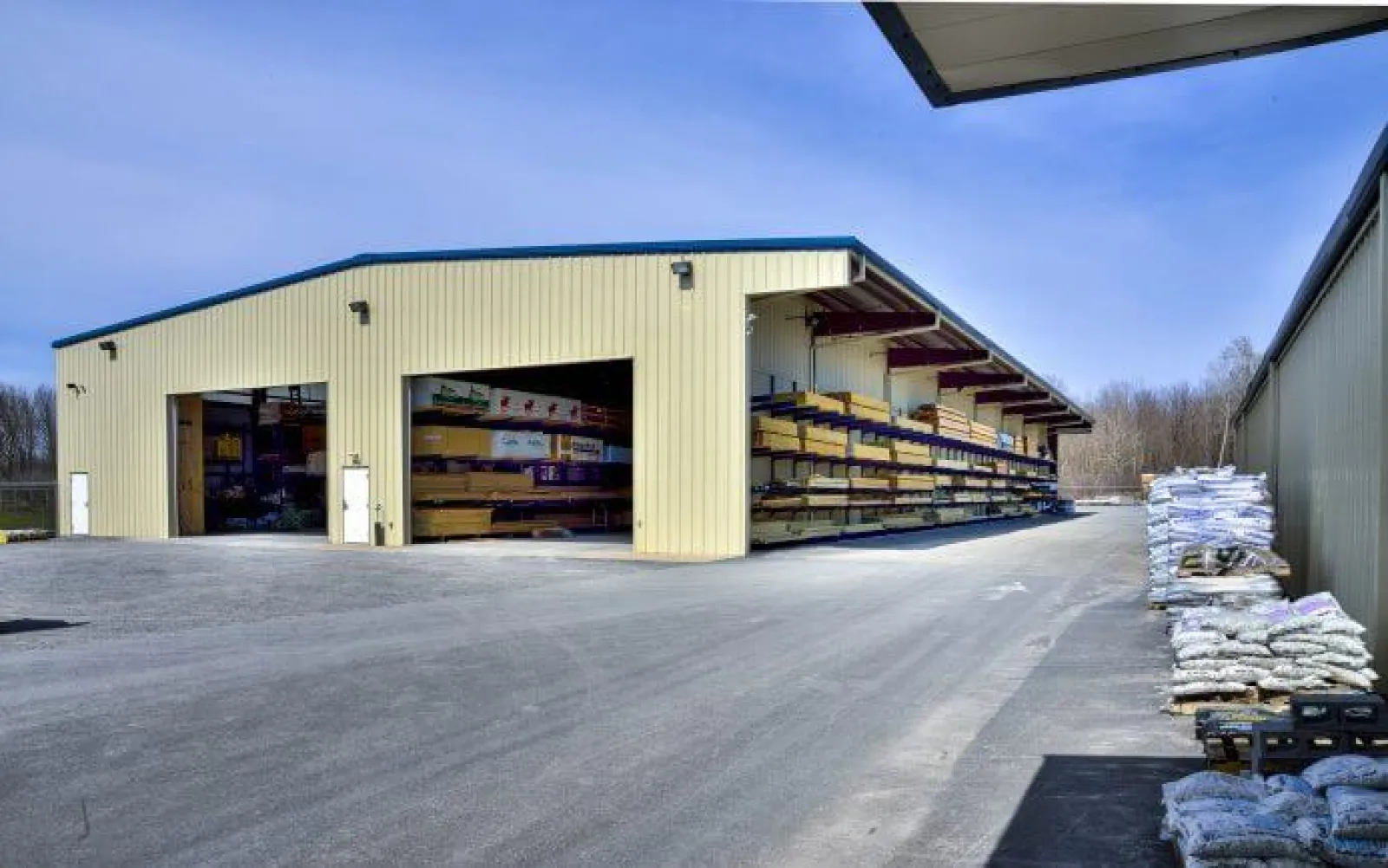 Warehouse building with open storage of lumber and bags of materials outside under clear blue sky