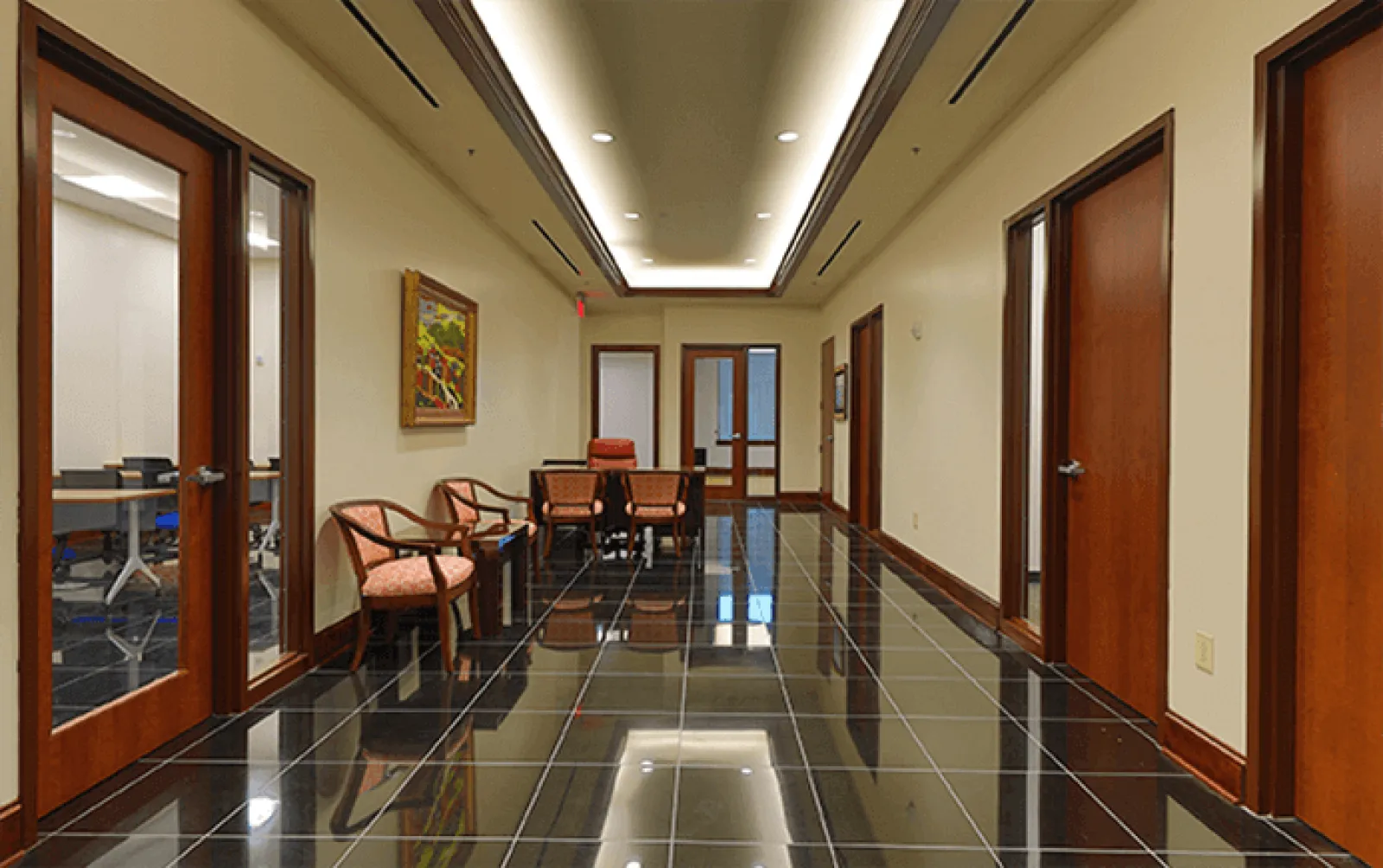 Modern hallway with glossy black tile floor, wooden doors, beige walls, chairs, and recessed ceiling lights.