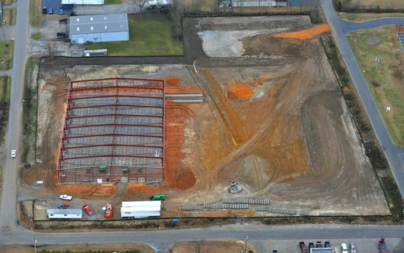 Aerial view of a construction site with steel framework erected and cleared land around it on a sunny day
