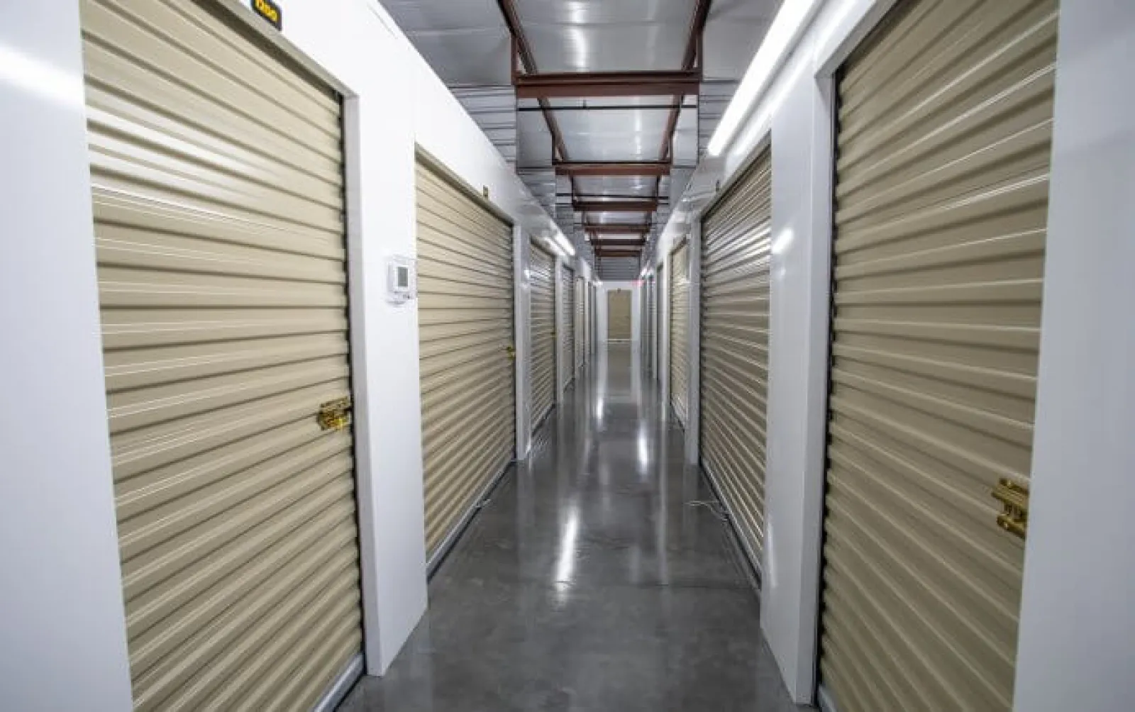 Indoor hallway of a storage facility with closed beige roll-up doors on both sides and polished concrete floor