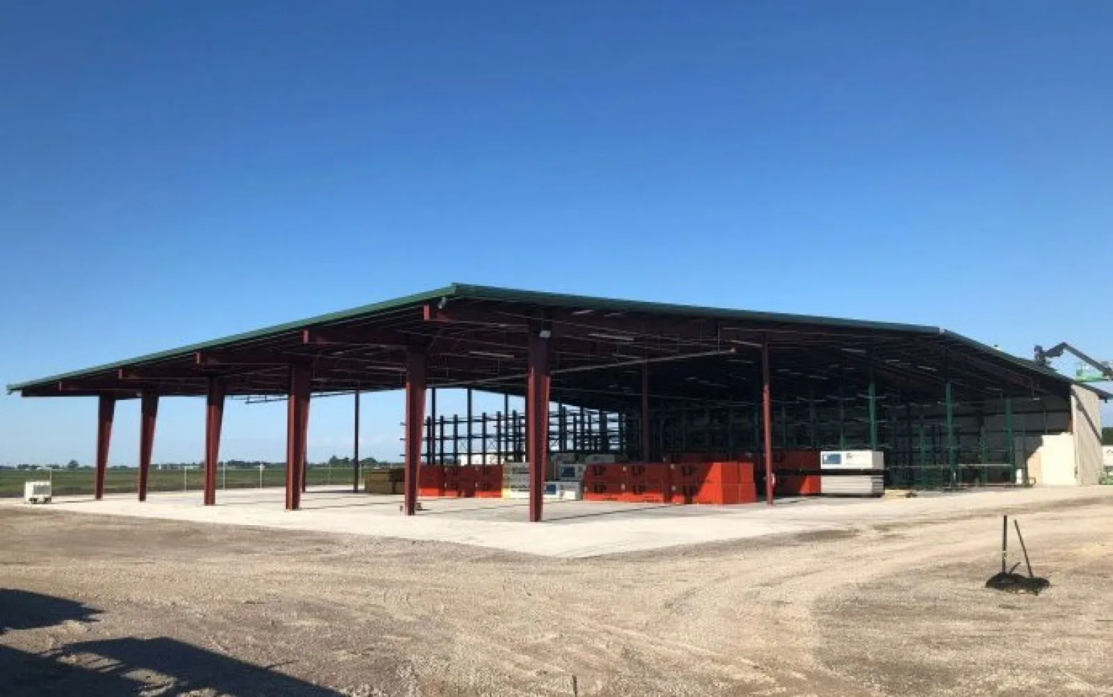 Steel-framed open warehouse under construction with a green roof on a clear sunny day in a rural area.