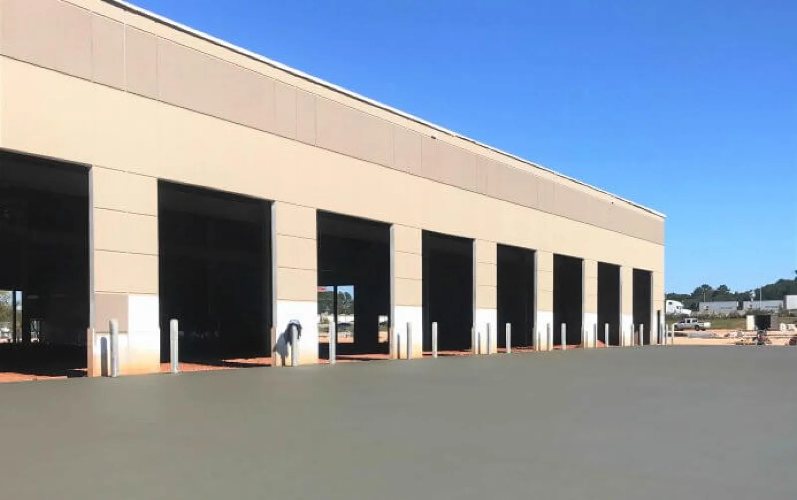 Exterior of a large industrial warehouse building with multiple wide open loading dock doors under a clear blue sky.