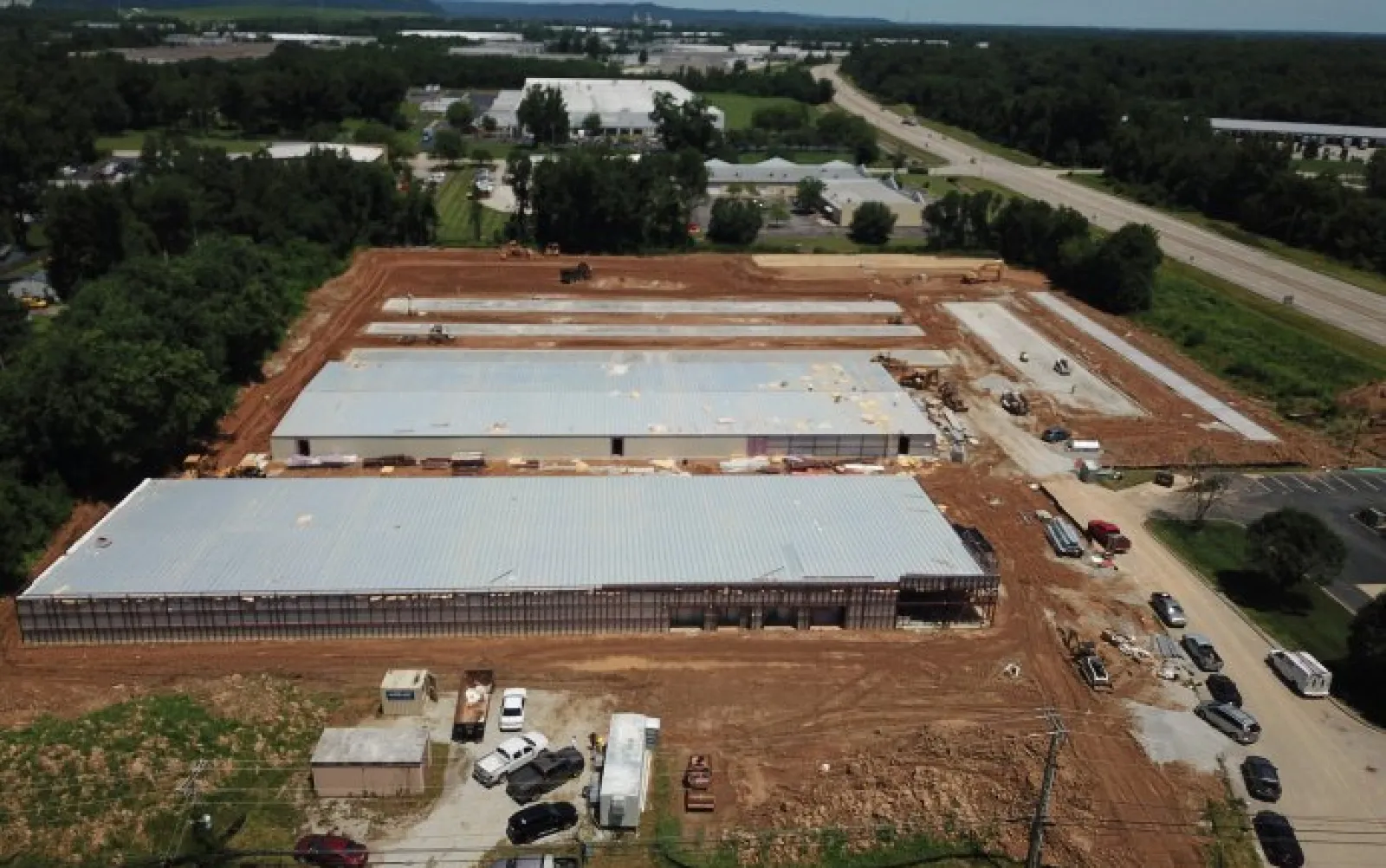 Aerial view of a large industrial warehouse construction site with metal roofs and surrounding cleared land.