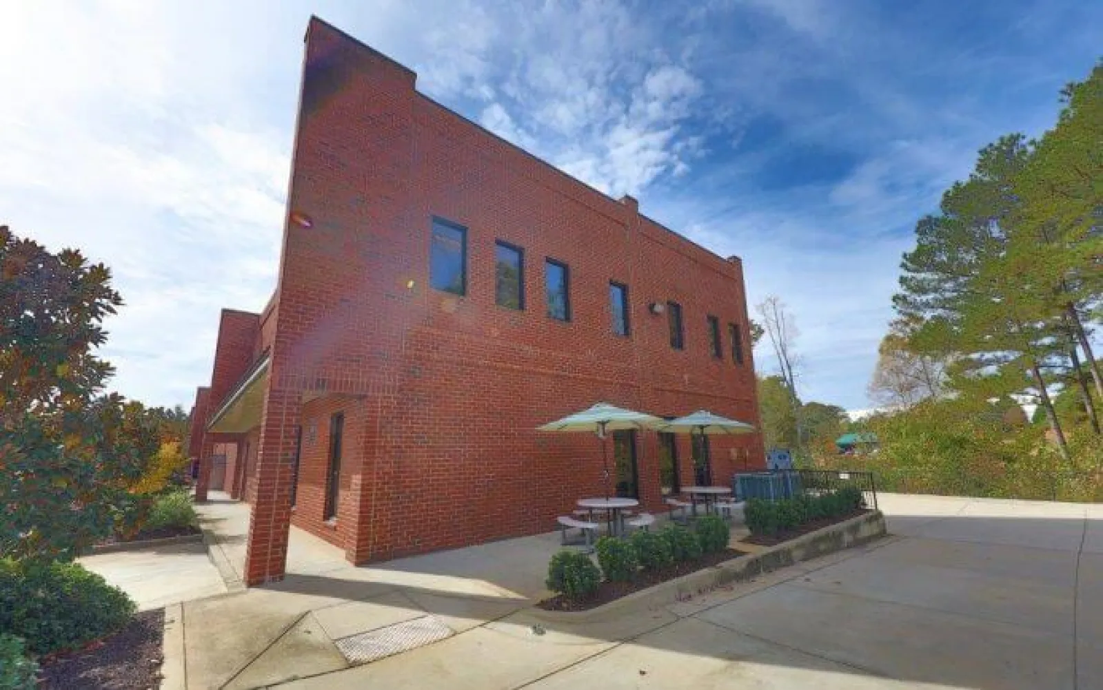 Two-story red brick building with outdoor seating umbrellas and tables under a partly cloudy sky.