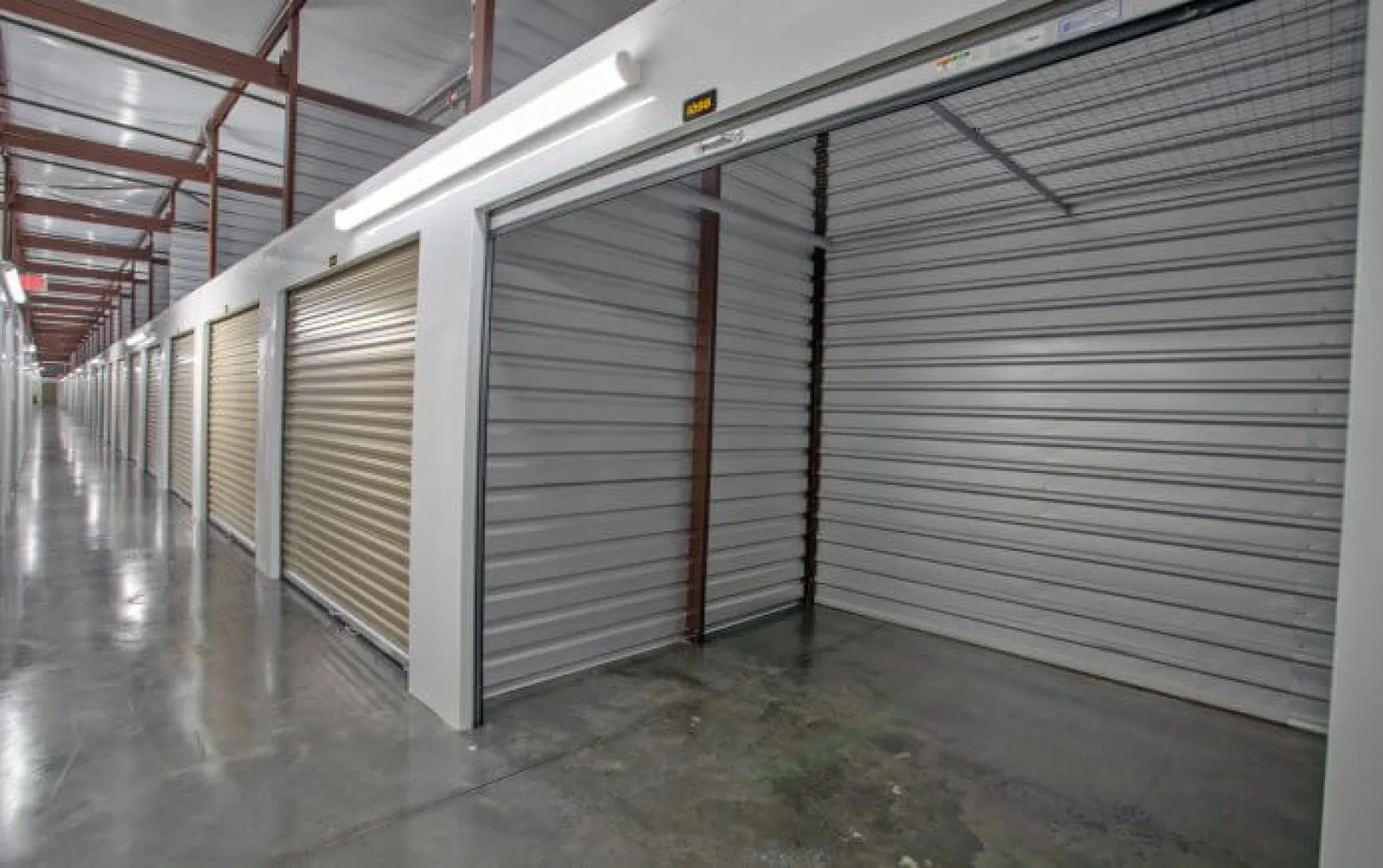 Interior view of a self-storage facility with open and closed metal roll-up doors and polished concrete floors.